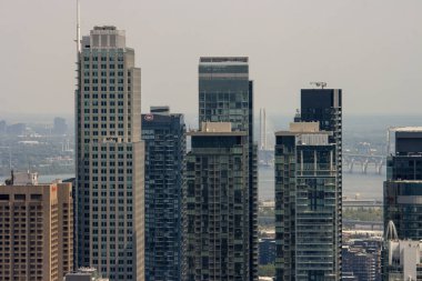 Kanada, 06 Temmuz 2025: Gökdelenler sisli yaz gökyüzünün altında nehir köprüsü üzerinde dimdik duruyorlar