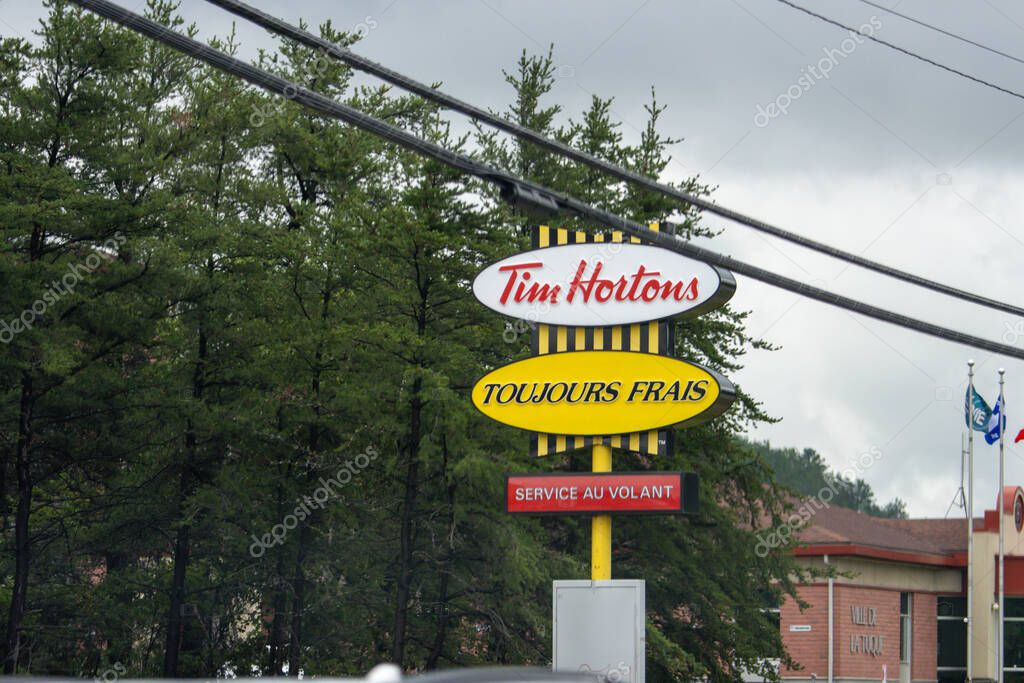 Quebec, Canada, 20 July 2025 : Tim Hortons sign in front of trees with cloudy skies overhead