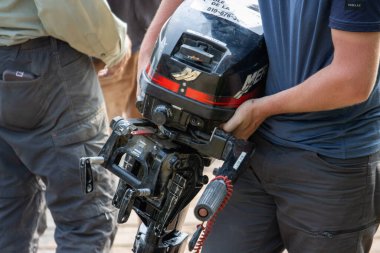 Kanada, 08 Ağustos 2025: Tekne motorunu arka planda insanlarla rıhtımda taşımak