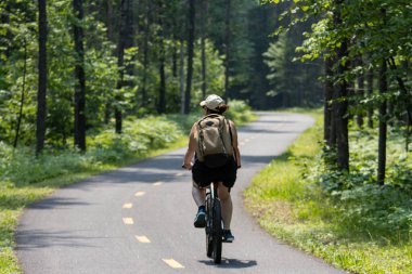 Quebec, Kanada, 15 Temmuz 2025: Bisikletçi güneşli yeşil orman yolunda huzur içinde bisiklet sürüyor