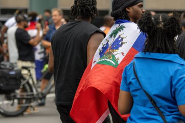 Quebec, Kanada, 05 Temmuz 2025: Canlı şehir toplantısında genç adam gururla Haiti bayrağına sarıldı