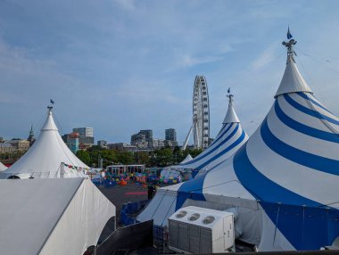 Kanada, 05 Temmuz 2025: Kentsel arka planda dönme dolabı olan mavi-beyaz sirk çadırları