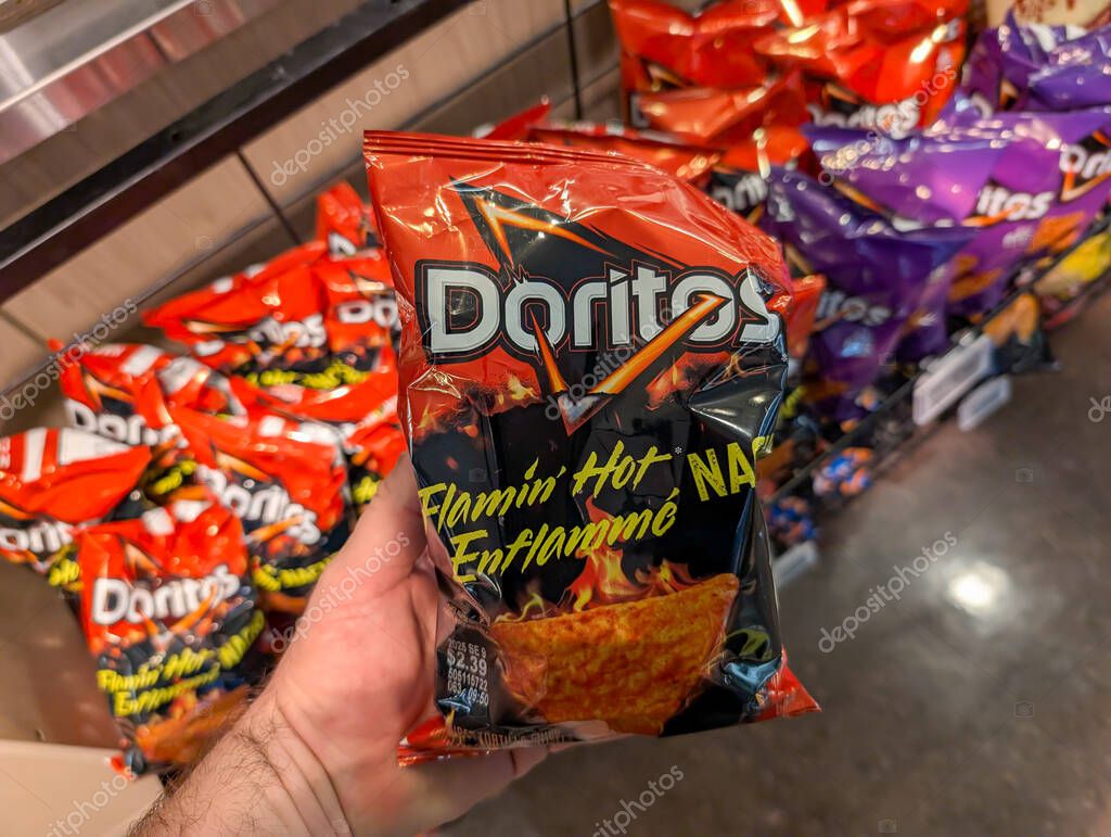 Quebec, Canada, 04 July 2025 : Hand holding Doritos flamin hot chips bag in store snack aisle.