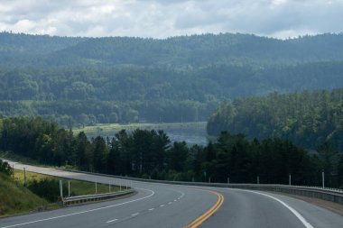 Quebec, Kanada, 20 Temmuz 2025: Bereketli ormanlarla çevrili sakin bir nehre uzanan kıvrımlı otoyol