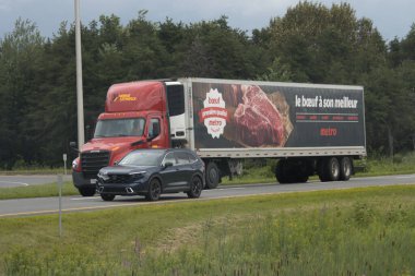 Quebec, Kanada, 20 Temmuz 2025: Biftek reklamı taşıyan kırmızı kamyon ve ardından siyah Honda aracı