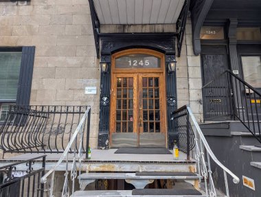 Quebec, Kanada, 06 Temmuz 2025: Cam kaplı kahverengi ahşap kapı, iki şişe, aşınmış beyaz adımlar