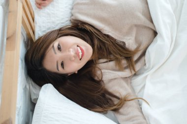 Portre güzel genç Asyalı kadın yatakta evde sabah. Neşeli Asyalı kadın yatağında gülen ve rahat bir kazak giyiyor. Oda rahatlatıcı. yaşam tarzı Asya kadın ev concept.