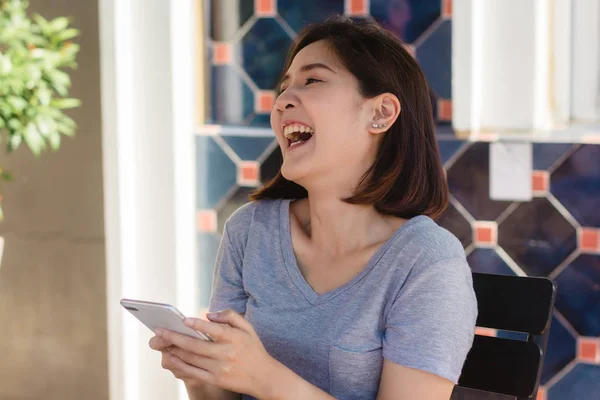 Iloinen Aasialainen Nuori Nainen Istuu Kahvilassa Älypuhelimella Puhumiseen Lukemiseen Tekstaamiseen — kuvapankkivalokuva