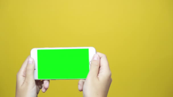女性は黄色のテーブル背景に緑色の画面でスマート フォンを使用します 女性の手のタッチ スクリーンをタップ スクロール ページ — ストック動画