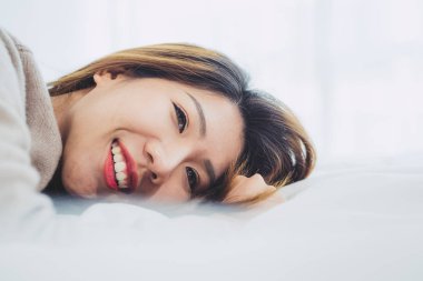 Portre güzel genç Asyalı kadın yatakta evde sabah. Neşeli Asyalı kadın yatağında gülen ve rahat bir kazak giyiyor. Oda rahatlatıcı. yaşam tarzı Asya kadın ev concept.