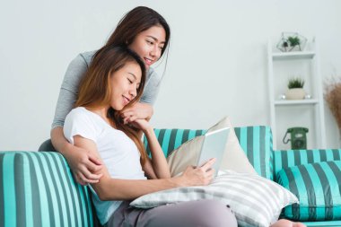 Kullanma online satın alma koltukta oturan güzel genç Asyalı kadınlar Lgbt lezbiyen mutlu çift evde oturma odasında tablet. LGBT lezbiyen birlikte kapalı kavramı çift. Evde güzel vakit.