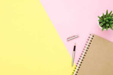Yaratıcı düz fotoğraf çalışma masası yatıyordu. Üstten Görünüm Ofis Masası ile defter ve kalem ve bitki pembe sarı pastel renk arka plan üzerine açık sahte. Kopya alanı, düz yatıyordu fotoğraf ile Üstten Görünüm.