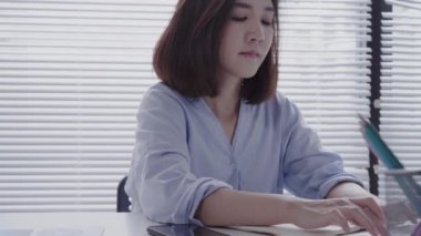 Güzel genç zorlanma Asyalı kadın evde oturma odasında otururken dizüstü bilgisayarda çalışıyor. Ev ofisinde çalışmak için telefon kullanarak Asya iş kadını. Evde zaman zevk.