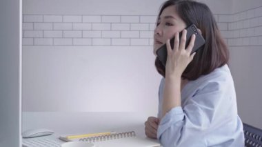 Evde oturma odasında otururken dizüstü bilgisayarda çalışma güzel genç gülümseyen Asyalı kadın. Ev ofisinde çalışmak için telefon kullanarak Asya iş kadını. Evde zaman zevk.