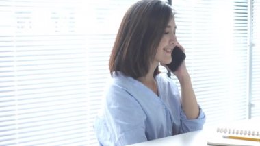 Evde oturma odasında otururken dizüstü bilgisayarda çalışma güzel genç gülümseyen Asyalı kadın. Ev ofisinde çalışmak için telefon kullanarak Asya iş kadını. Evde zaman zevk.