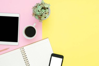 Ofis Masası adlı kullanıcının alanı - düz çalışma boş defter sayfası, kahve fincanı ve sahte telefon tablet pastel arka plan üzerinde yukarı çalışma alanının en iyi görünümü yatırın. Pastel pembe sarı renk arka plan boşluk kavramı.