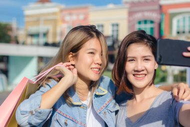 Şehirde alışveriş yaparken bir smartphone kullanarak çekici güzel Asyalı kadın. Mutlu Genç Asyalı Genç arkadaşları ile birlikte bir akıllı telefon ile kendi portreleri çekerken kentsel City.