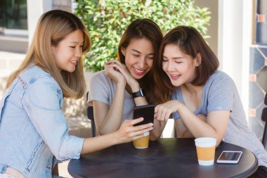 Arkadaş grubu kahve içme ve birlikte konuşurken kafede oturan neşeli Asyalı Genç kadınlar. Kahve için konuşma, okuma ve manifatura smartphone kullanırken zevk çekici Asyalı kadın.