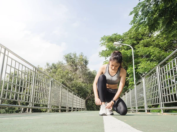 Close up of young woman lace up her shoe ready to workout on exercising in the park with warm light sunshine in morning. Young woman prepare for outdoor exercise in park. Outdoor exercise concept.