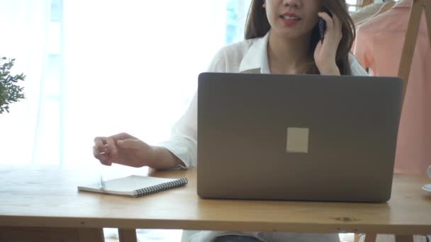 慢动作 美丽的年轻微笑的亚洲妇女在笔记本电脑上工作 而坐在家里的起居室 在她的家庭办公室使用电话工作的亚洲商业妇女 在家享受时光 — 图库视频影像