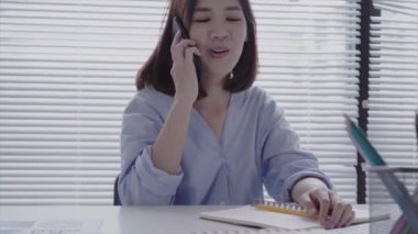 Evde oturma odasında otururken dizüstü bilgisayarda çalışma güzel genç gülümseyen Asyalı kadın. Ev ofisinde çalışmak için telefon kullanarak Asya iş kadını. Evde zaman zevk.