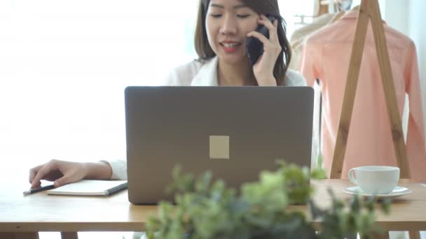 美しい若い笑顔アジア女性の自宅のリビング ルームに座っているラップトップに取り組んで アジア ビジネスの女性は 彼女の家のオフィスで仕事の電話を使用して 家での時間を楽しんでください — ストック動画
