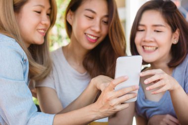 Arkadaş grubu kahve içme ve birlikte konuşurken kafede oturan neşeli Asyalı Genç kadınlar. Kahve için konuşma, okuma ve manifatura smartphone kullanırken zevk çekici Asyalı kadın.
