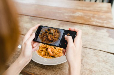 Kadın blogger telefonunu restoranda öğle fotoğraf çekme. Spagetti yemek yemek Mobil kamera ile fotoğraf çekme Smartphone cep telefonu ile bir genç kadın alarak fotoğraf.