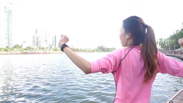 慢动作 亚洲美女在健身套装正在使用一个 Smartwatch 听音乐 在电话后 在公园里跑步 有吸引力的健康女性慢跑 — 图库视频影像