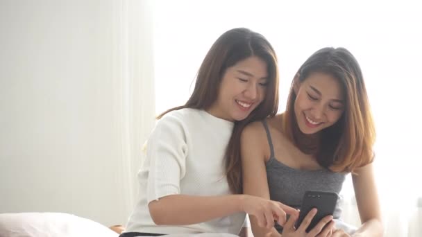 美丽的年轻亚裔女性同志同性恋快乐夫妇坐在床上拥抱和使用电话在一起卧室在家里 同志夫妇一起在室内的概念 在家度过美好的时光 — 图库视频影像