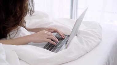 Güzel Asyalı kadın yatak odasında yatağın üstüne yalan sırasında bilgisayar ya da laptop oynamak. Mutlu kadın evde alışveriş online satın alma. Yaşam tarzı kadına ev concept. 