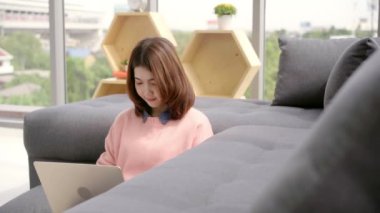 Genç Asyalı kadın araştırma çalışmaları için onu iş yapıyor. Online alışveriş web sitesi tarama yaparken rahatlatıcı kanepede oturan kadın gülümsüyor. Mutlu kız evde serbest zaman sırasında internet üzerinden tarama.