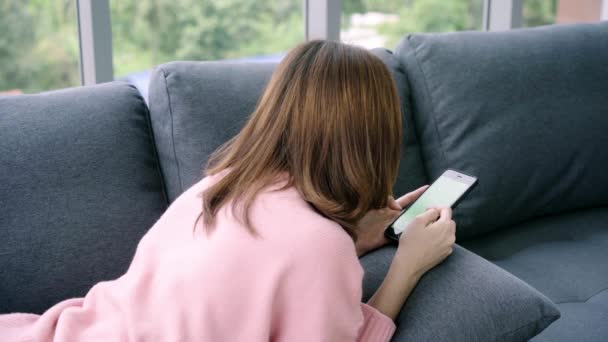 年轻的亚洲妇女使用黑色智能手机设备与绿色屏幕 亚洲妇女手持电话 在客厅的沙发上滚动页面 色度键 — 图库视频影像