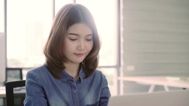 美丽微笑的年轻亚洲商人的肖像坐在明亮的现代工作站上 并在办公室打字笔记本电脑 — 图库视频影像