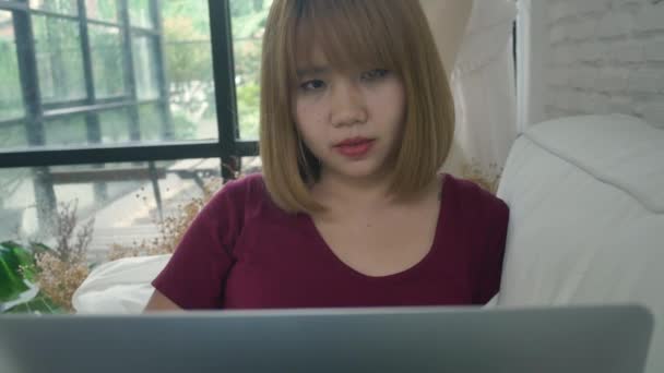 为她的事业做研究工作的年轻亚洲妇女 微笑的女人坐在沙发上放松 而浏览网上购物网站 快乐的女孩在家里的空闲时间浏览互联网 — 图库视频影像