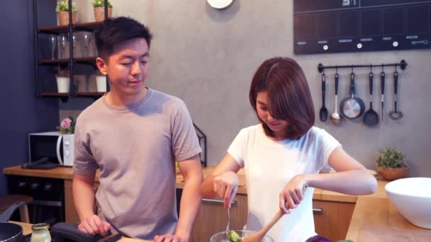 アジアの女性は 台所でサラダ調理します 美しい幸せなアジア カップル台所で調理しています 若いアジアのカップルは 自宅に滞在しながらロマンチックな時間を持っています ホーム コンセプトでカップルのライフ スタイル — ストック動画