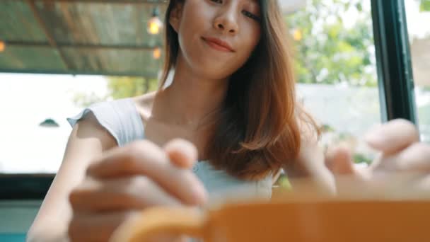 陽気なアジア若い女性は温かいコーヒーやカフェに座って楽しんでお茶を飲んだします 一杯のコーヒーを保持している魅力的な幸せなアジア女 — ストック動画