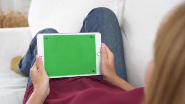 若いアジアの女性は 緑色の画面で黒いタブレット デバイスを使用して リビング ルームのソファに座りながらページをスクロールするタブレットを保持しているアジア女性 クロマ — ストック動画