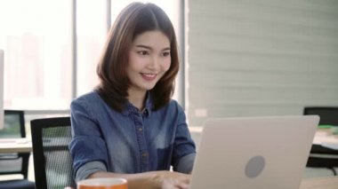 Ofiste smartphone kullanarak tadını çıkarırken dizüstü bilgisayarda çalışma güzel genç gülümseyen Asyalı kadın. Ev ofis belge finans çalışan Asya iş kadın. Ofiste zaman zevk.