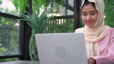 Oturma odasında evde dizüstü bilgisayarda çalışan güzel genç gülümseyen Asya Müslüman kadın. Belge finans ve hesap makinesi ev ofisinde çalışan Asya iş kadın. Evde zaman zevk.