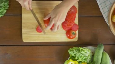 Salata sağlıklı yemek yapma ve mutfakta kesme tahtası üzerinde domates doğrama kadın baş üstten görünüm.