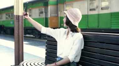 Mutlu Asyalı kadın yolcu ile rahat alarak selfie tarafından akıllı cep telefonu Tren İstasyonu raylar Bangkok şehir, Tayland seyahat için. yaşam tarzı ve ulaşım kavramı.
