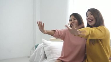 Mutlu Asya lezbiyen lgbt çift oturma odası eğlencenin keyfine varın. Güzel kadınlar bir koltukta yalan smartphone evde müzik dinlemek.