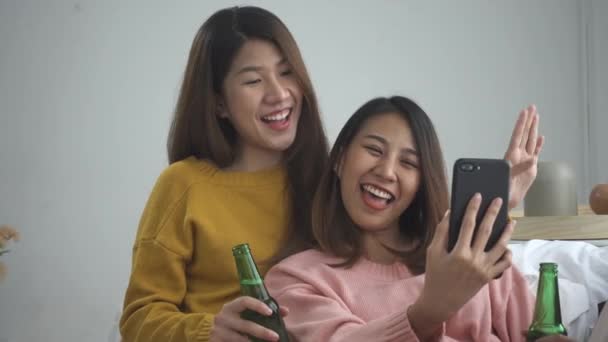 快乐的亚洲女同性恋同志夫妇坐在沙发上喝啤酒和使用智能手机在起居室 妇女在家庆祝与她的女朋友 — 图库视频影像