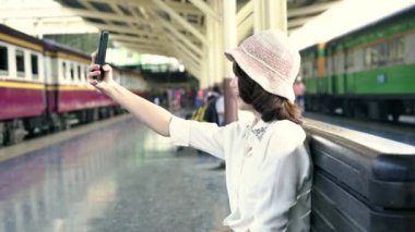 Mutlu Asyalı kadın yolcu ile rahat alarak selfie tarafından akıllı cep telefonu Tren İstasyonu raylar Bangkok şehir, Tayland seyahat için. yaşam tarzı ve ulaşım kavramı.