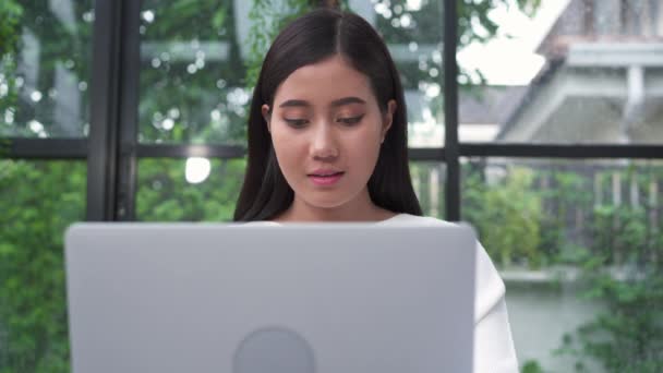 美しい若い笑顔アジア女性の自宅のリビング ルームで座っている間のラップトップに取り組んで アジア ビジネスの女性は 作業文書金融とホーム オフィスの計算機 家での時間を楽しんでください — ストック動画