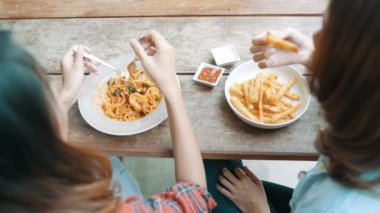 Her tarafı ise gülümseyen ve yiyecek arayan bir tabak İtalyan deniz mahsulleri spagetti ve patates kızartması restoran ya da kafe yemek oturan güzel mutlu Asyalı kadınlar lezbiyen lgbt çift.