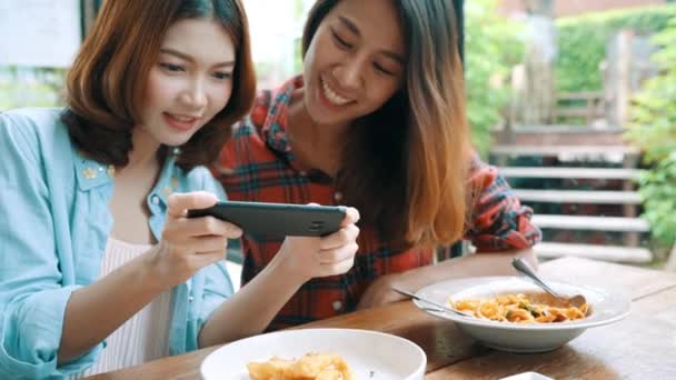 スマート フォンの写真を使用しての彼女の加入者とのカフェでの彼女のチャネルのビデオ食品ビデオブログを作る幸せな美しいアジアの友人女性ブロガー — ストック動画