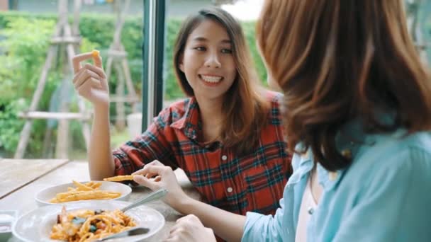 微笑みながら見て料理イタリアン シーフード スパゲッティとレストランやカフェでフライド ポテトのプレートを食べてそれぞれの側に座って美しい幸せなアジア女性レズビアン Lgbt カップル — ストック動画