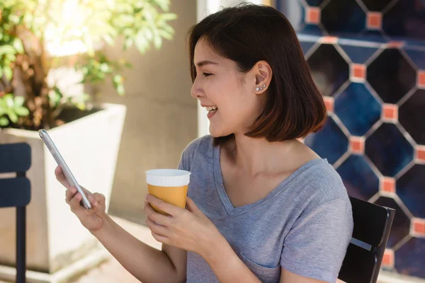 Iloinen Aasialainen Nuori Nainen Istuu Kahvilassa Juomassa Kahvia Käyttämällä Älypuhelinta — kuvapankkivalokuva